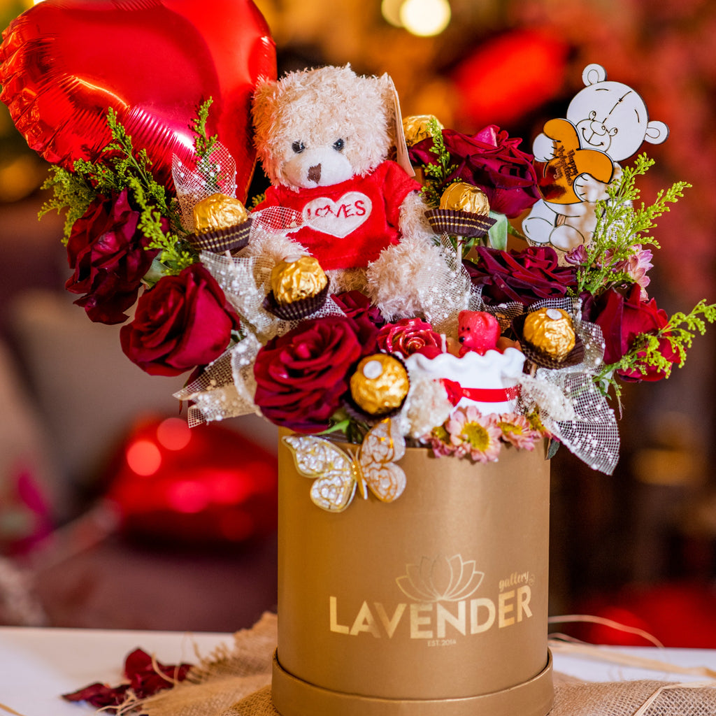 Decorative flower arrangement with a teddy bear, heart-shaped balloon, and 'LAVENDER' branding.